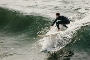 man in black wet suit riding white surfboard on green sea during daytime